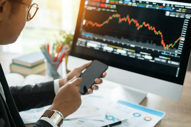 Trader with a smartphone, trading chart on the computer's screen